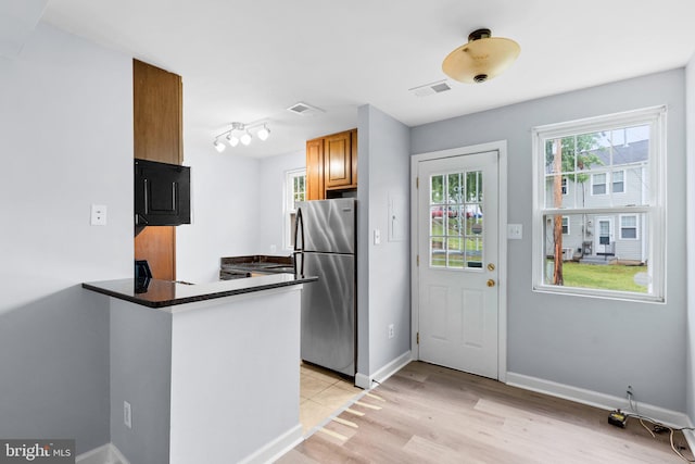 kitchen featuring stainless steel fridge, kitchen peninsula, dark stone counters, and light hardwood / wood-style flooring