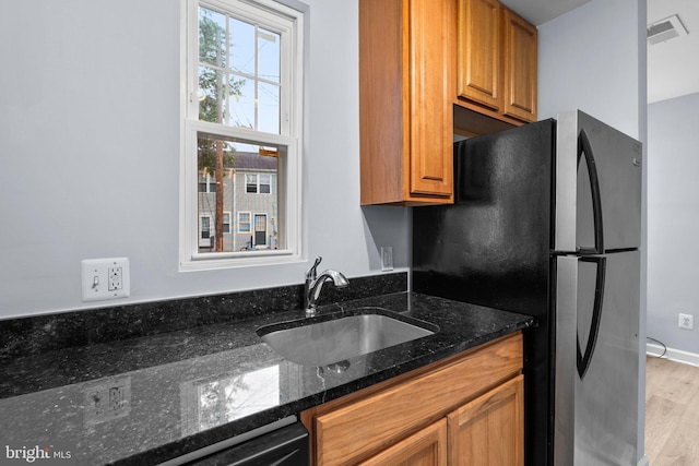 kitchen featuring black refrigerator, light wood-type flooring, dark stone counters, dishwashing machine, and sink