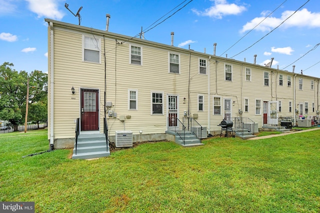 rear view of property featuring central AC unit and a lawn