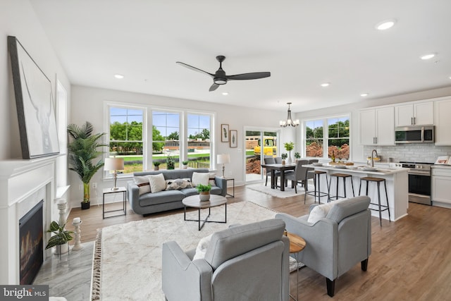 living room with plenty of natural light, sink, light wood-type flooring, and ceiling fan with notable chandelier