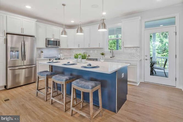 kitchen featuring pendant lighting, white cabinets, light wood-type flooring, appliances with stainless steel finishes, and a kitchen island