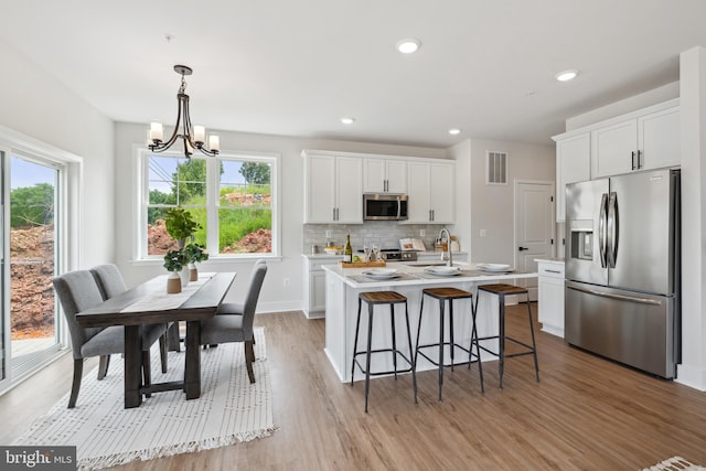 kitchen featuring appliances with stainless steel finishes, a chandelier, pendant lighting, white cabinets, and light wood-type flooring