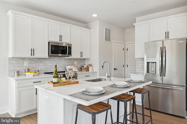 kitchen with stainless steel appliances, a center island with sink, light hardwood / wood-style flooring, white cabinets, and a breakfast bar area