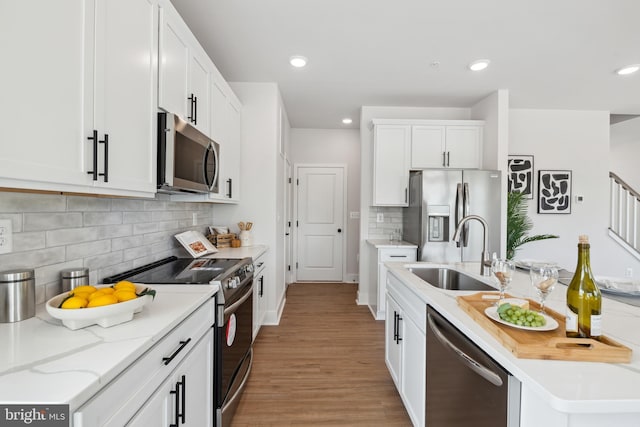 kitchen with appliances with stainless steel finishes, light wood-type flooring, backsplash, sink, and white cabinetry