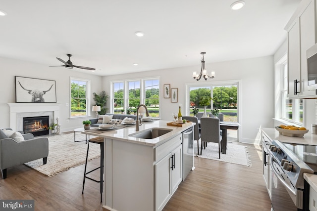 kitchen with a kitchen island with sink, white cabinets, dark hardwood / wood-style floors, decorative light fixtures, and stainless steel appliances