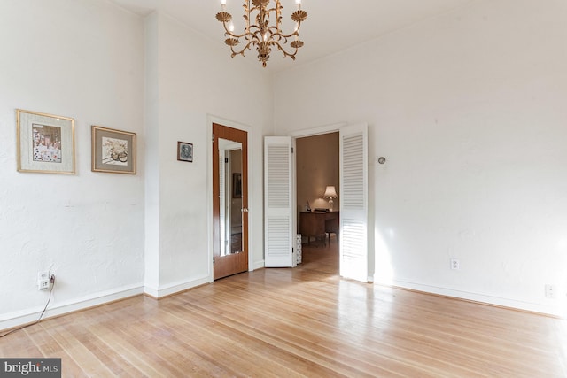 spare room with a towering ceiling, light hardwood / wood-style floors, and an inviting chandelier