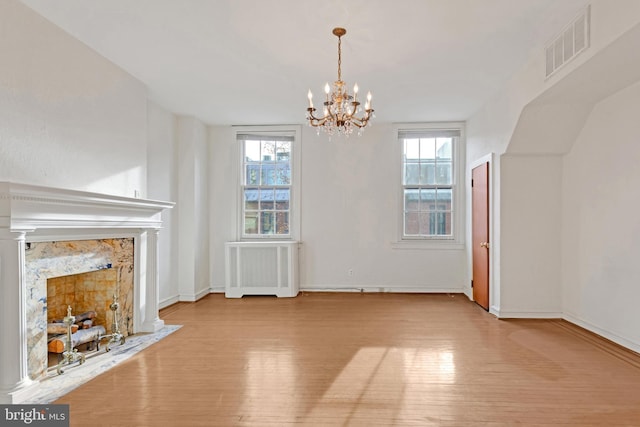 unfurnished living room with radiator, light hardwood / wood-style flooring, a healthy amount of sunlight, and a fireplace