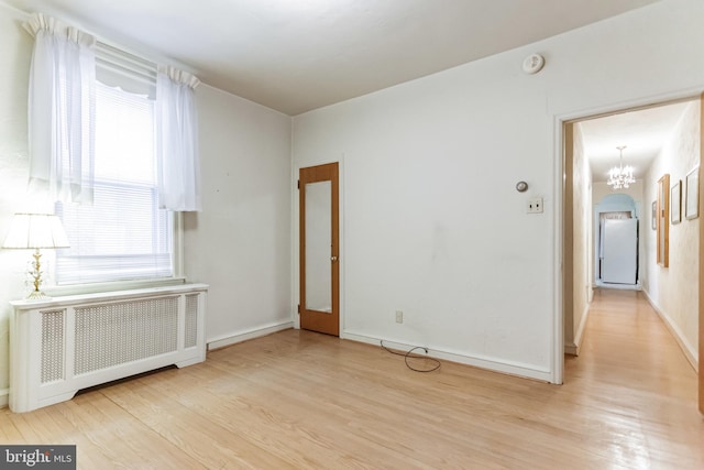 unfurnished room featuring a chandelier, radiator heating unit, light hardwood / wood-style flooring, and a wealth of natural light