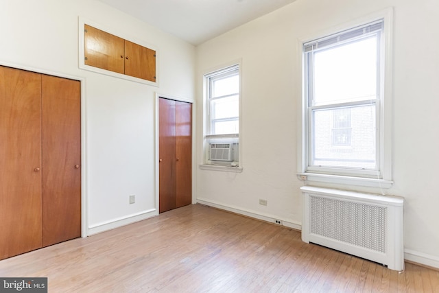 unfurnished bedroom with radiator heating unit, light wood-type flooring, and cooling unit