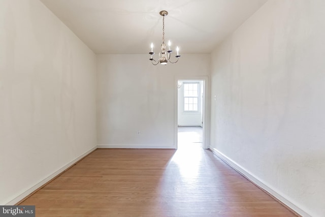 unfurnished room with a notable chandelier and light wood-type flooring