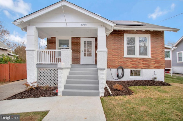 bungalow-style home featuring a front lawn, solar panels, and a porch