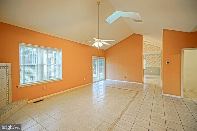 spare room with a fireplace, light tile patterned floors, lofted ceiling with skylight, and ceiling fan