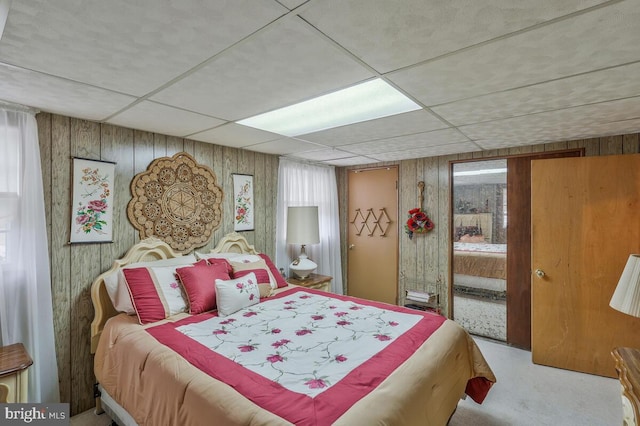 carpeted bedroom featuring wood walls and a drop ceiling