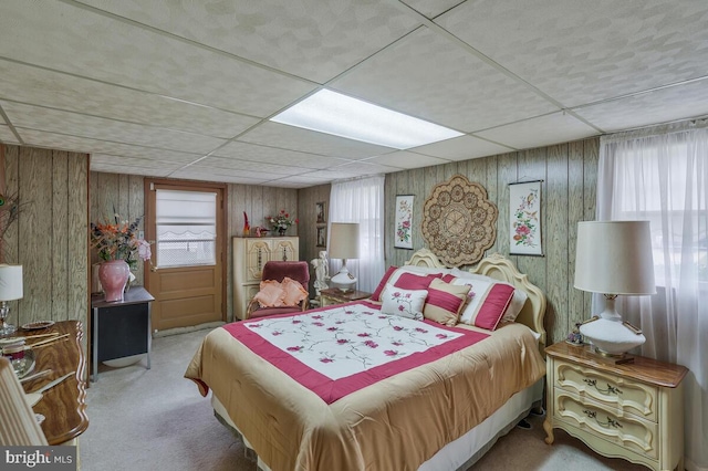 bedroom with light carpet, a drop ceiling, and wood walls