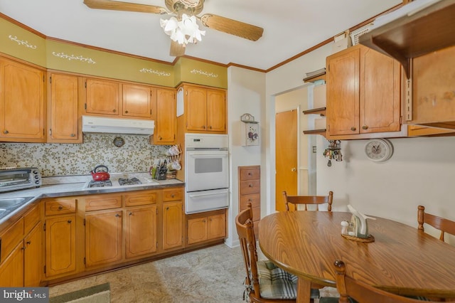 kitchen with ceiling fan, stainless steel gas cooktop, oven, decorative backsplash, and ornamental molding