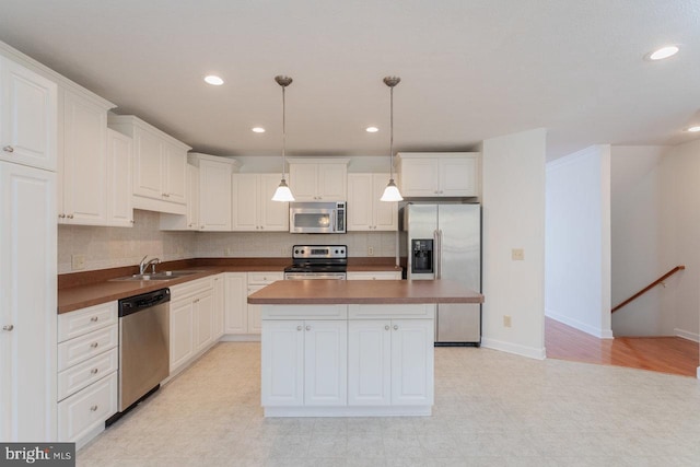 kitchen with white cabinetry, sink, hanging light fixtures, stainless steel appliances, and a kitchen island