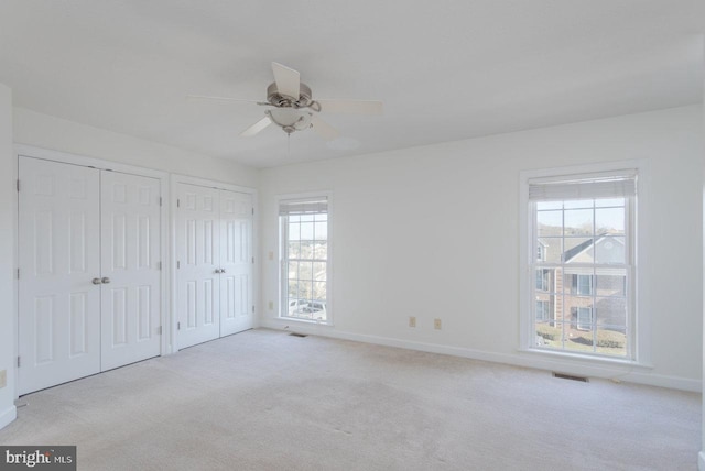 unfurnished bedroom with ceiling fan, two closets, light carpet, and multiple windows