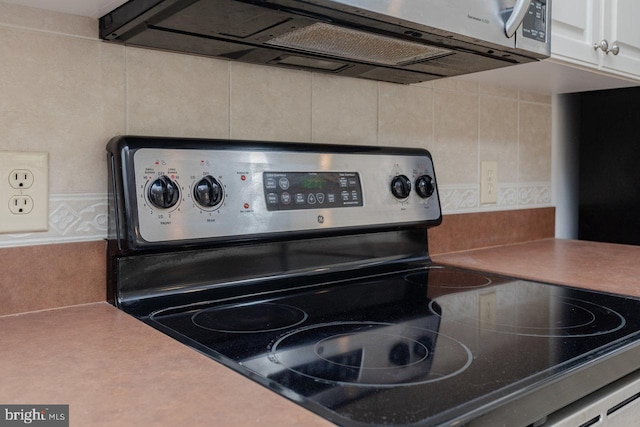 kitchen featuring white cabinets, electric range oven, and tile walls