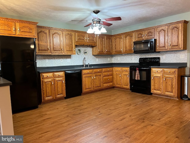 kitchen with a textured ceiling, ceiling fan, sink, black appliances, and light hardwood / wood-style floors