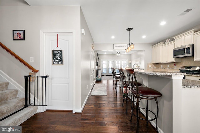 kitchen with light stone counters, stainless steel appliances, ceiling fan, dark wood-type flooring, and pendant lighting