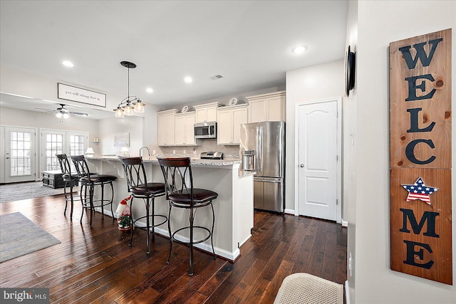 kitchen with light stone countertops, stainless steel appliances, ceiling fan, dark wood-type flooring, and a center island with sink