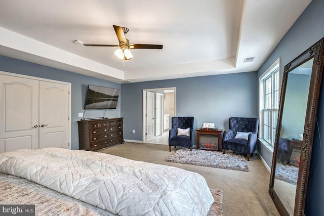 bedroom featuring a tray ceiling, ceiling fan, a closet, and light carpet