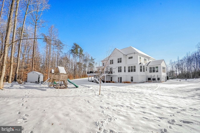 snow covered back of property featuring a storage unit and a playground