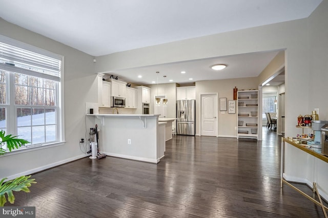 kitchen with kitchen peninsula, appliances with stainless steel finishes, a healthy amount of sunlight, white cabinets, and a breakfast bar area