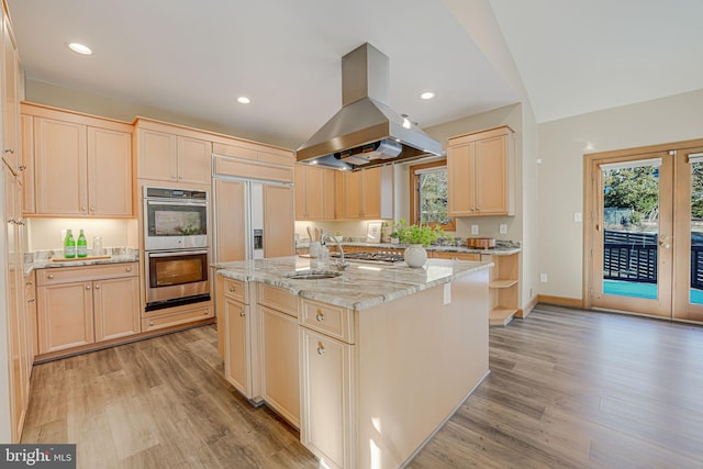 kitchen with sink, appliances with stainless steel finishes, light stone counters, island range hood, and an island with sink