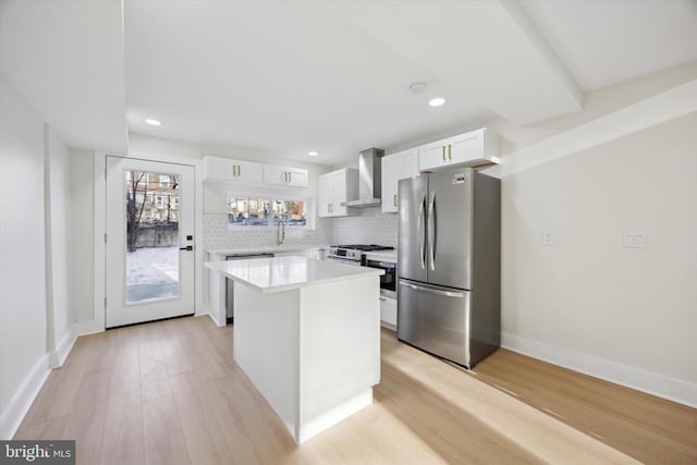 kitchen featuring white cabinetry, a center island, wall chimney range hood, light hardwood / wood-style floors, and appliances with stainless steel finishes