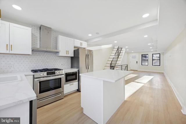 kitchen with tasteful backsplash, white cabinets, wall chimney exhaust hood, and appliances with stainless steel finishes