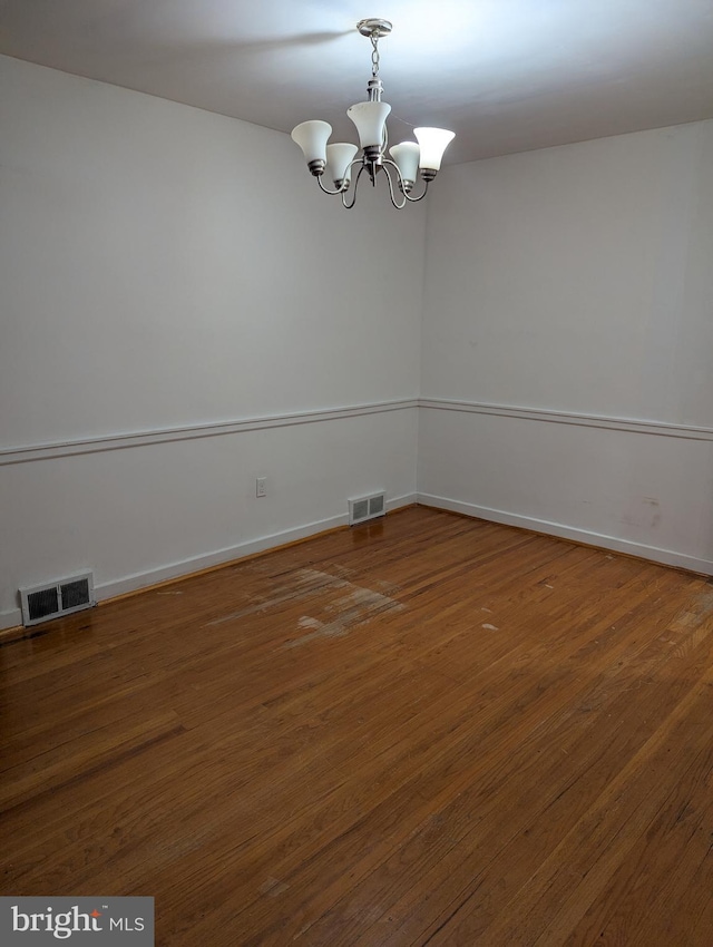 empty room featuring dark wood-type flooring and a chandelier