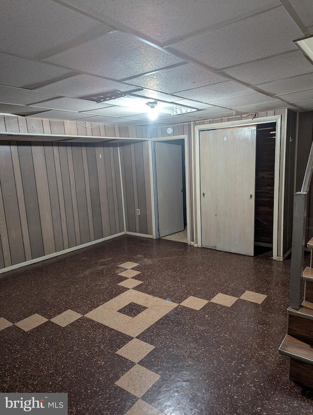 basement with a drop ceiling and wood walls