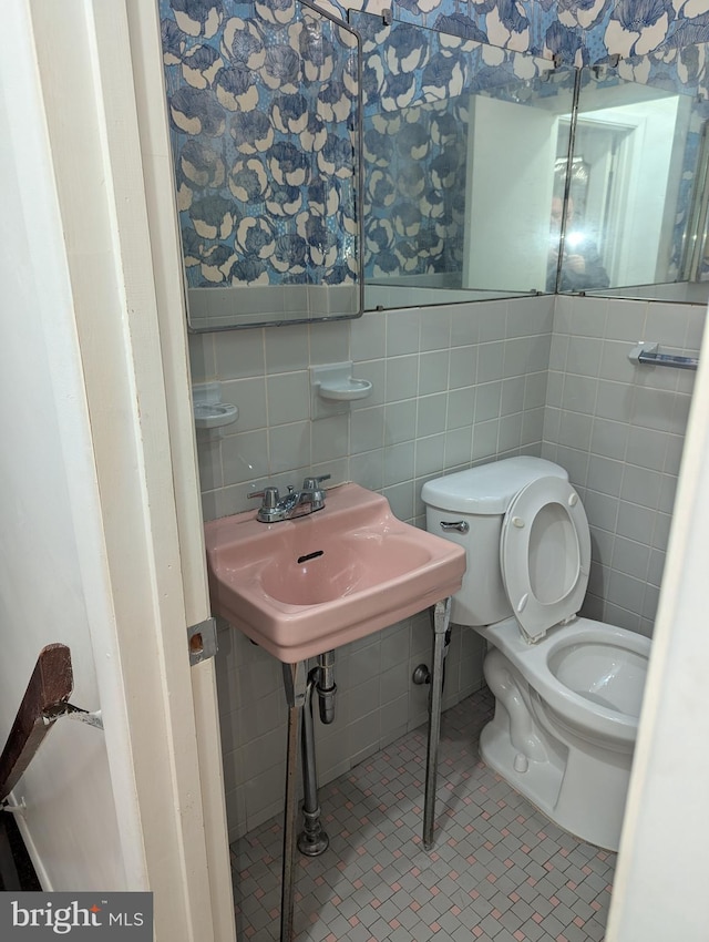 bathroom with toilet, tile patterned floors, and tile walls