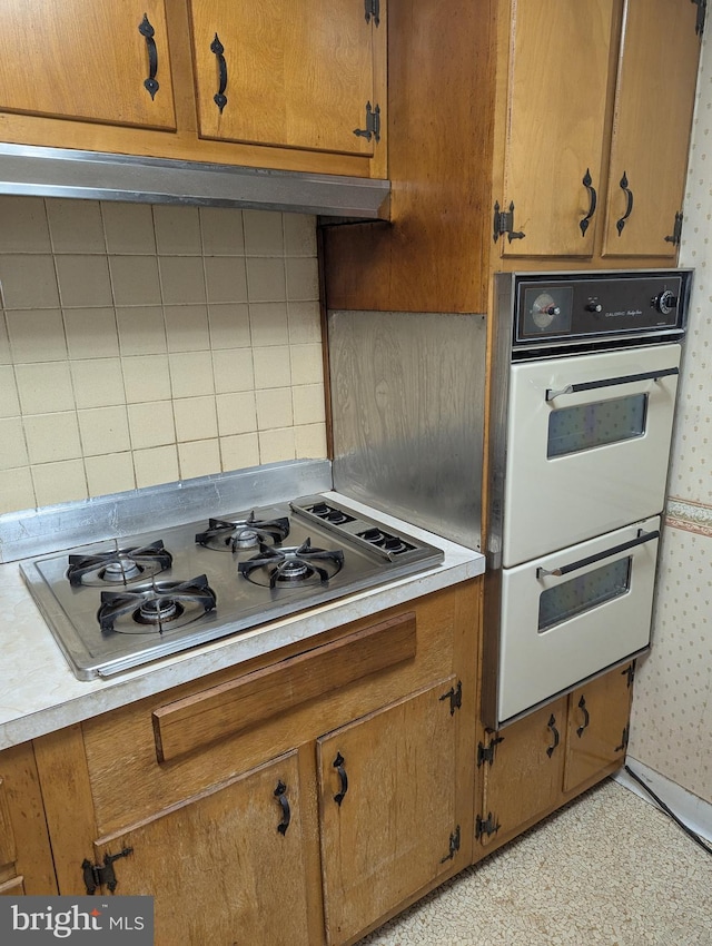 kitchen featuring white double oven, tasteful backsplash, extractor fan, and stainless steel gas stovetop