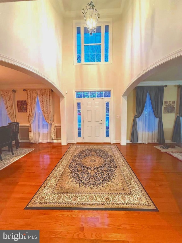 foyer entrance featuring hardwood / wood-style flooring, a notable chandelier, crown molding, and a high ceiling