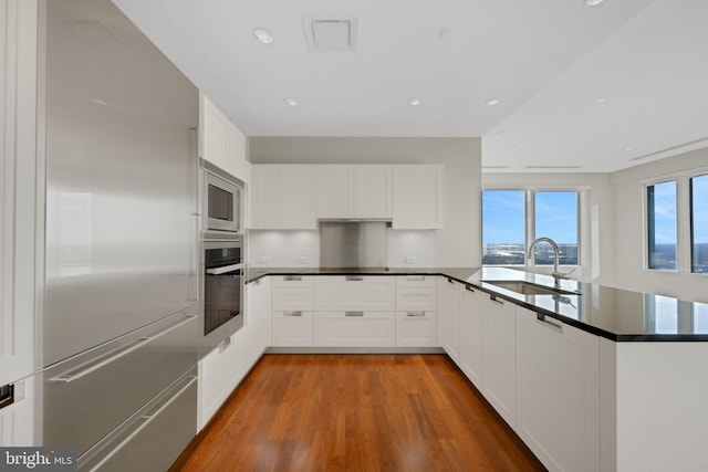 50 S 16th St Unit 5102, Philadelphia, PA 19102 - kitchen featuring a sink, built in appliances, light wood finished floors, a peninsula, and dark countertops