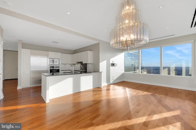 kitchen with hanging light fixtures, stainless steel appliances, a chandelier, white cabinets, and light wood-type flooring