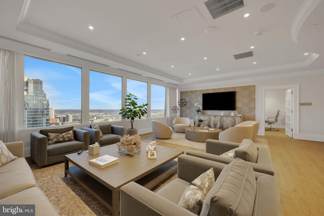 living room featuring light hardwood / wood-style floors, ornamental molding, and a tray ceiling