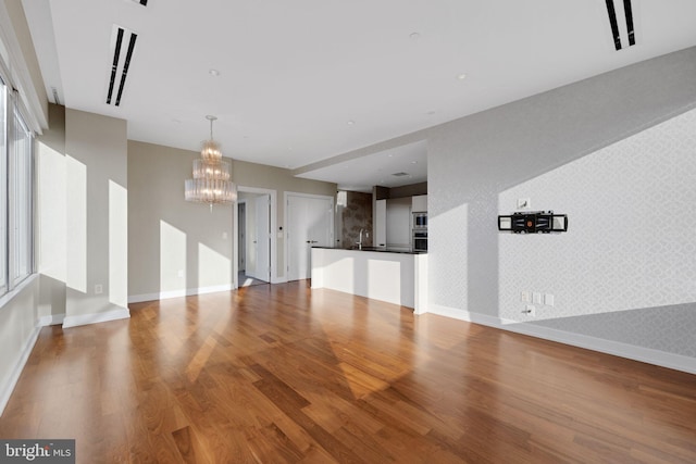 50 S 16th St Unit 5102, Philadelphia, PA 19102 - unfurnished living room with a chandelier, wood finished floors, baseboards, wallpapered walls, and a sink