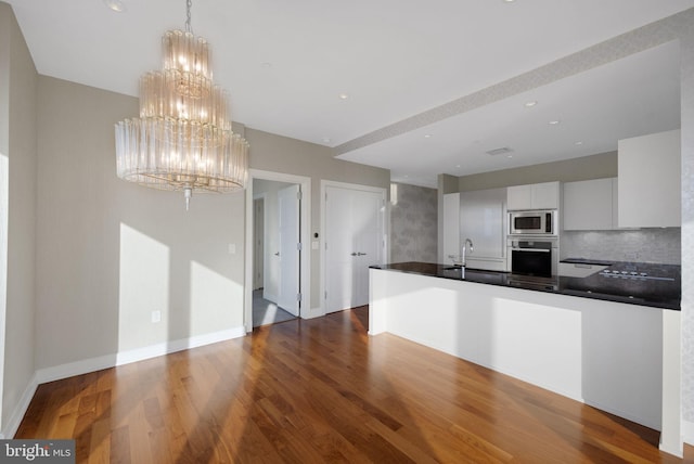 kitchen featuring appliances with stainless steel finishes, backsplash, a notable chandelier, white cabinets, and dark hardwood / wood-style floors