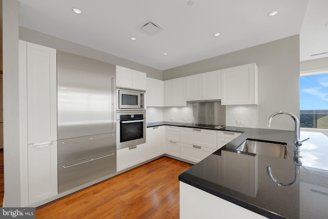 kitchen featuring light wood-type flooring, tasteful backsplash, stainless steel appliances, sink, and white cabinets