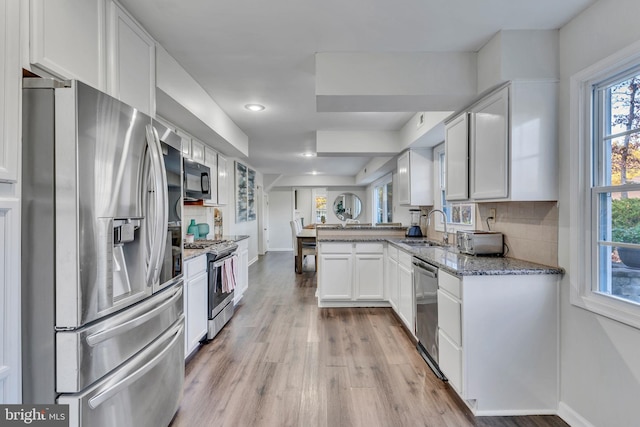 kitchen featuring light stone countertops, white cabinetry, sink, stainless steel appliances, and kitchen peninsula