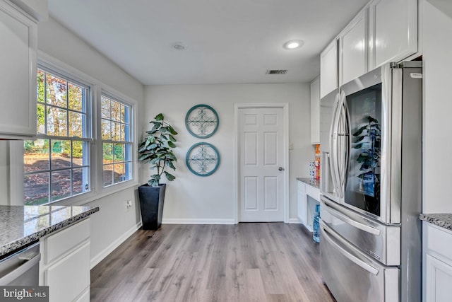 kitchen with appliances with stainless steel finishes, light wood-type flooring, stone countertops, and white cabinetry