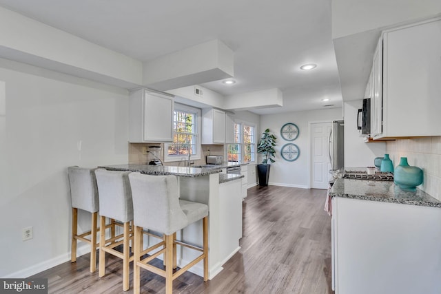 kitchen with white cabinetry, kitchen peninsula, dark stone counters, a breakfast bar area, and light wood-type flooring