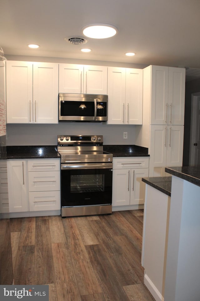 kitchen featuring white cabinets, dark hardwood / wood-style flooring, appliances with stainless steel finishes, and dark stone counters