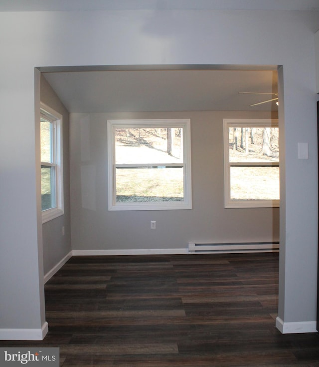 empty room with baseboard heating, a wealth of natural light, and dark wood-type flooring