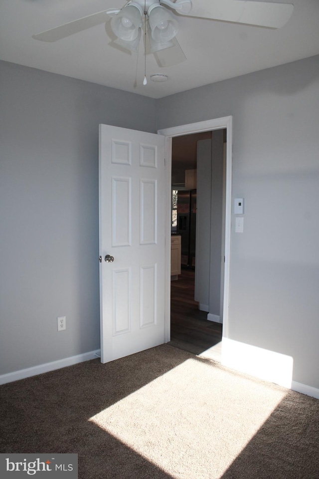 empty room featuring ceiling fan and dark carpet