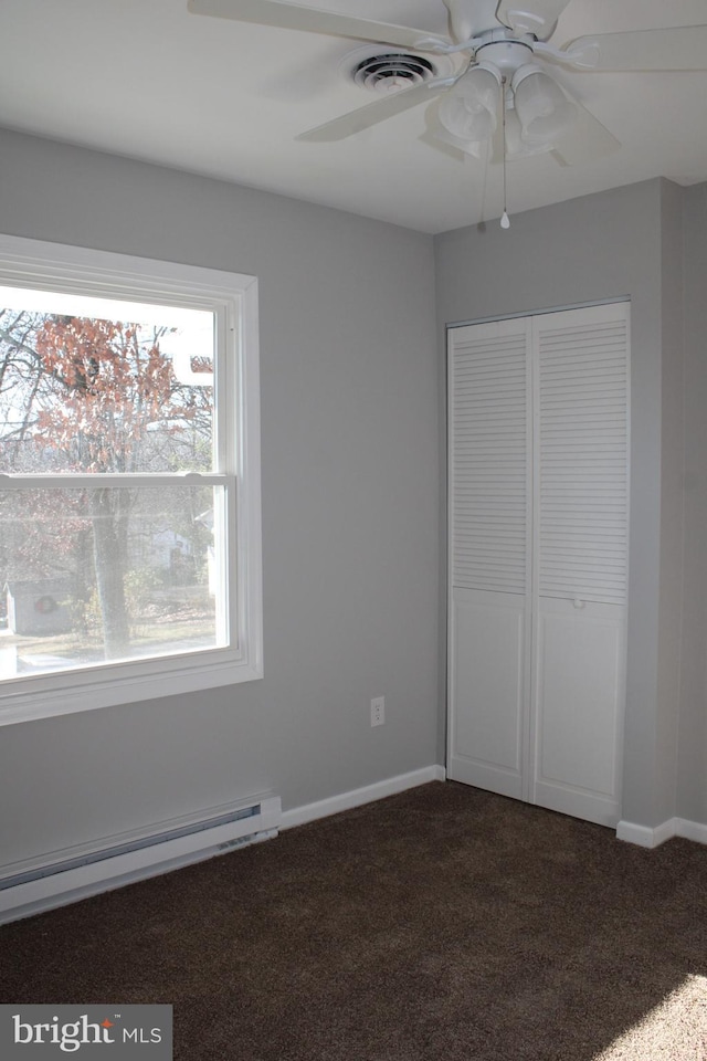 unfurnished bedroom with ceiling fan, dark carpet, a closet, and a baseboard radiator