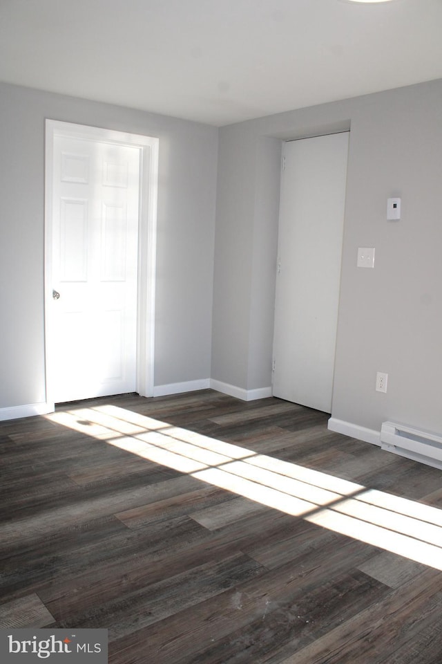 empty room featuring baseboard heating and dark wood-type flooring